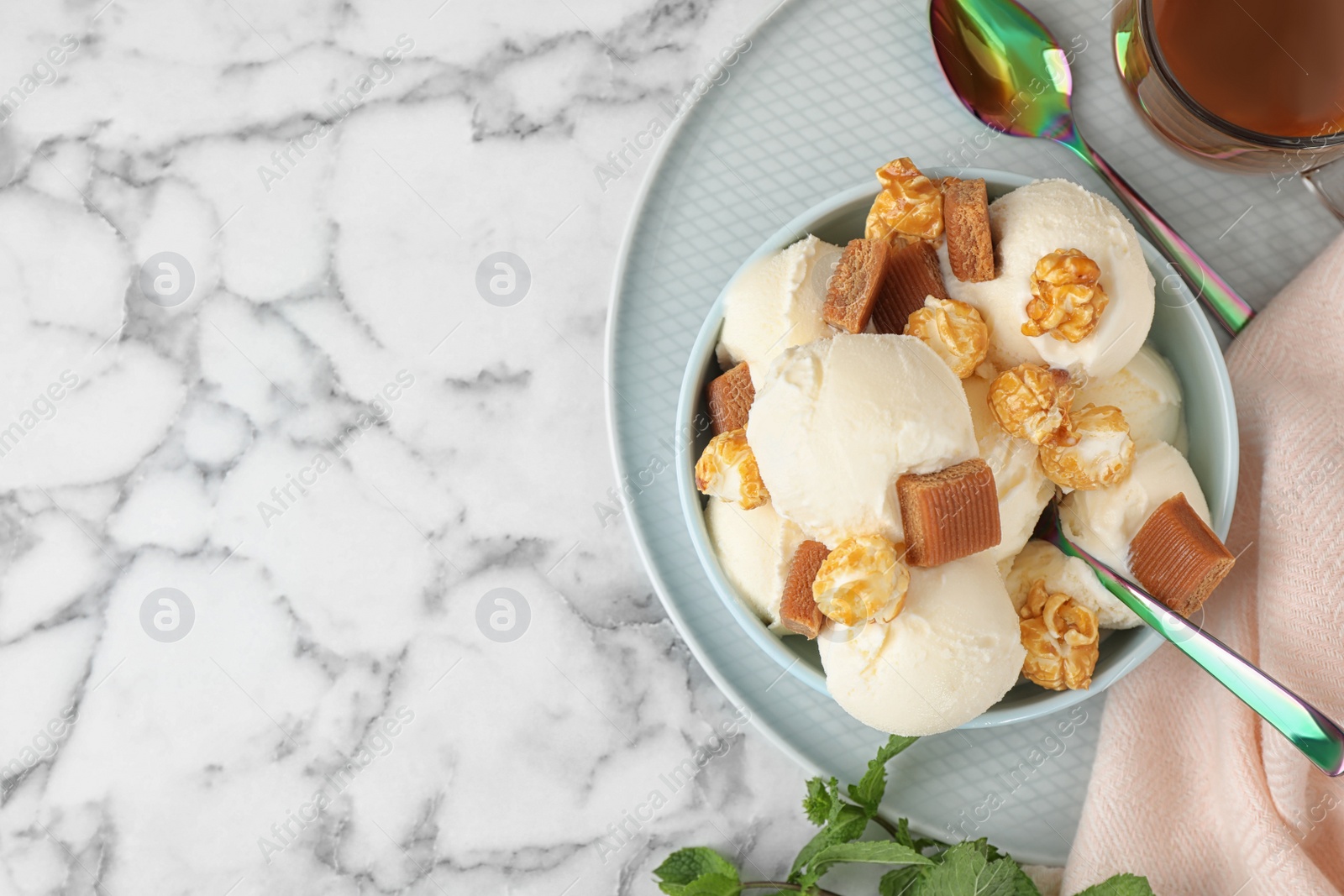 Photo of Plate of delicious ice cream with caramel candies and popcorn on white marble table, flat lay. Space for text
