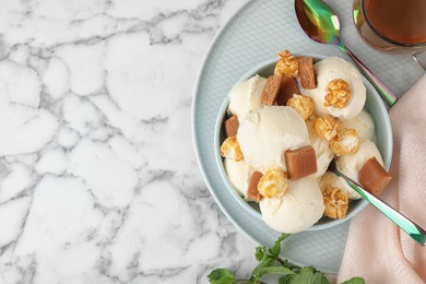 Plate of delicious ice cream with caramel candies and popcorn on white marble table, flat lay. Space for text
