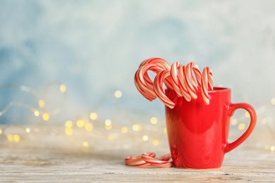 Photo of Tasty Christmas candy canes in cup on table. Space for text