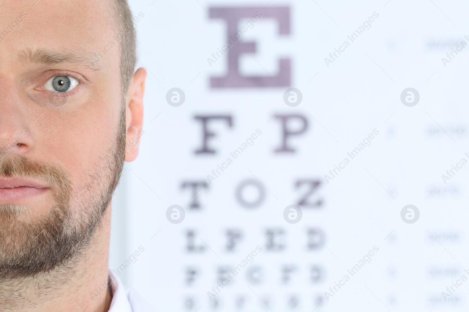 Photo of Closeup view of man and blurred eye chart on background. Space for text