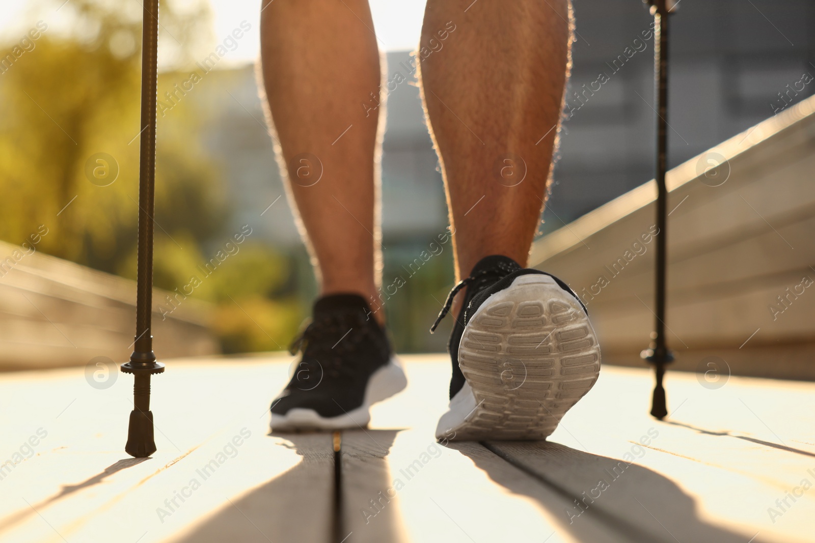 Photo of Man practicing Nordic walking with poles outdoors on sunny day, closeup