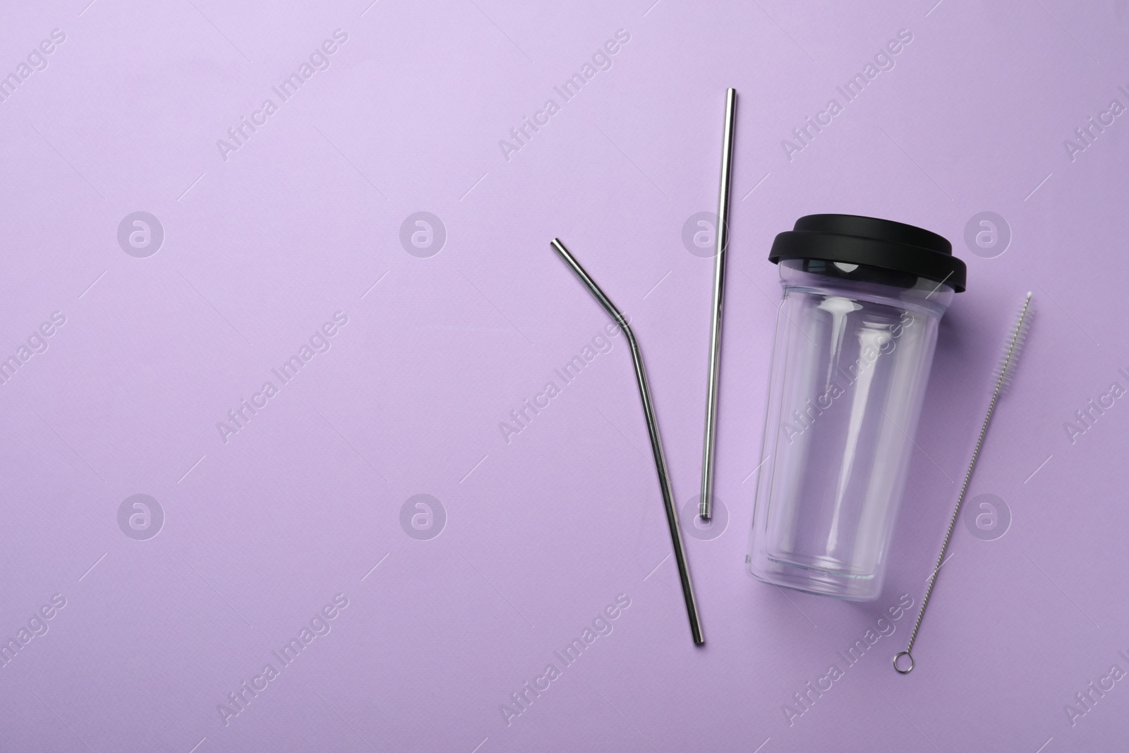 Photo of Glass cup, metal straws and brush on violet background, flat lay with space for text. Conscious consumption