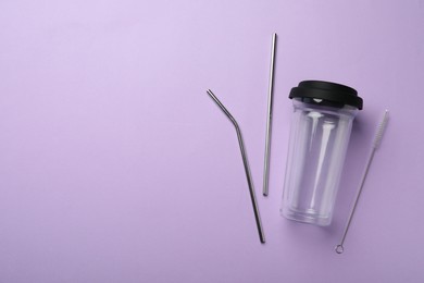 Glass cup, metal straws and brush on violet background, flat lay with space for text. Conscious consumption