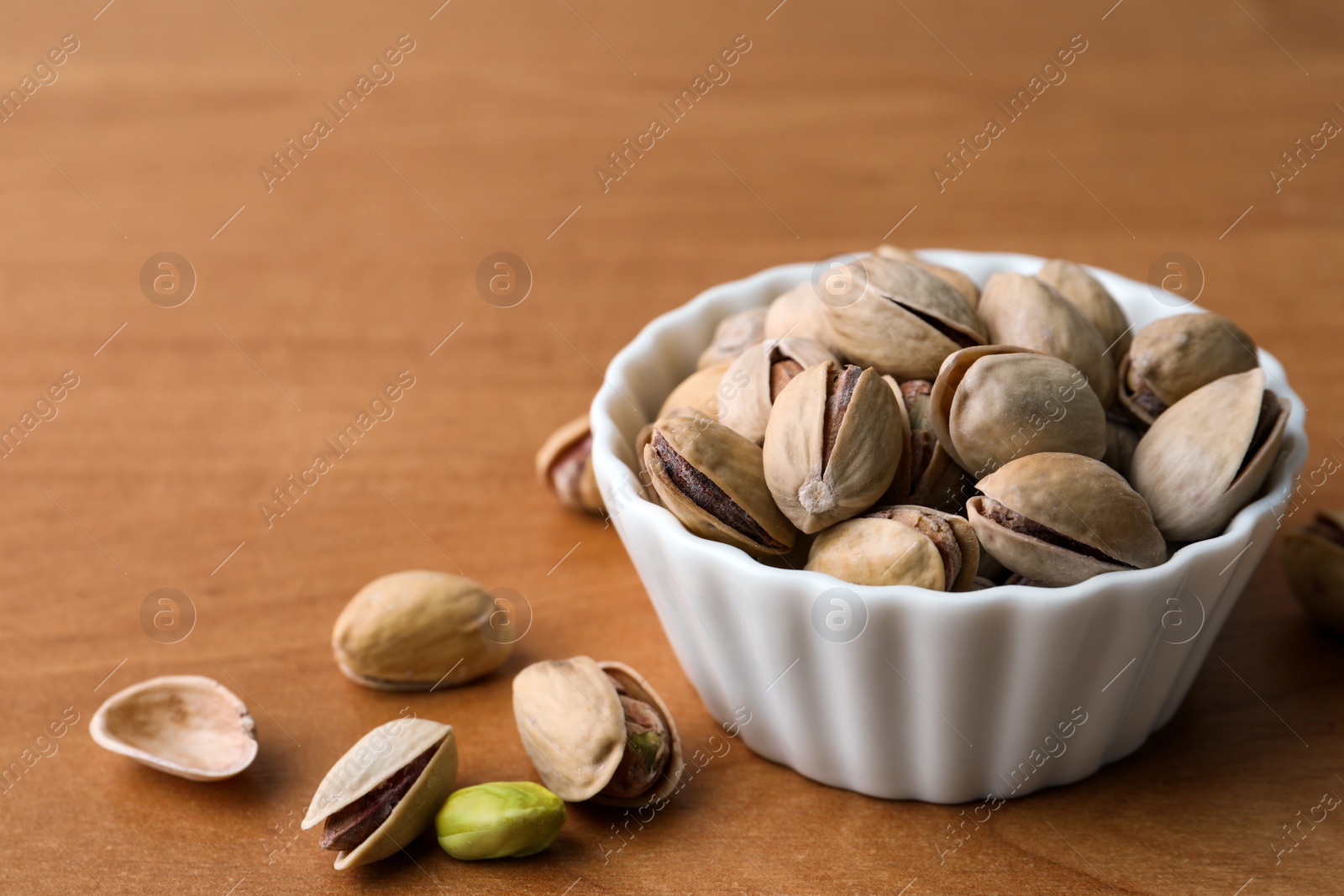 Photo of Bowl and pistachio nuts on wooden table, closeup