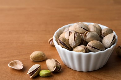 Bowl and pistachio nuts on wooden table, closeup