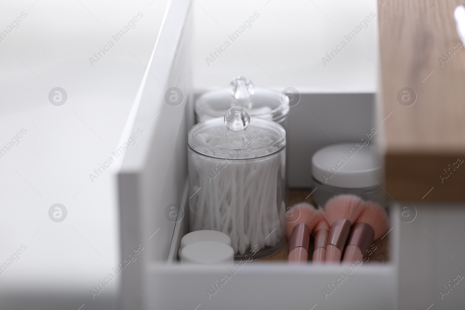Photo of Cotton buds, pads, creams and makeup brushes in open drawer