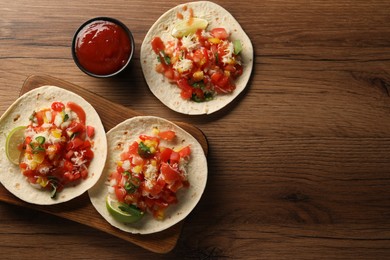 Photo of Delicious tacos with vegetables, lime and ketchup on wooden table, flat lay. Space for text