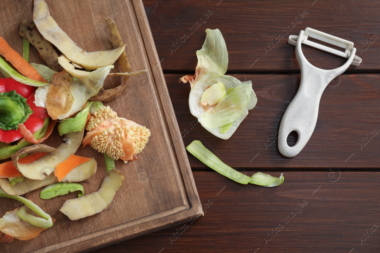 Photo of Peels of fresh vegetables and peeler on wooden table, flat lay