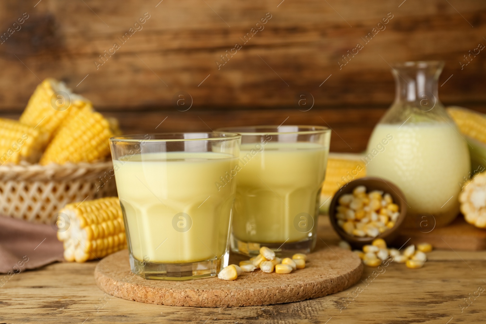 Photo of Tasty fresh corn milk in glasses and cobs on wooden table