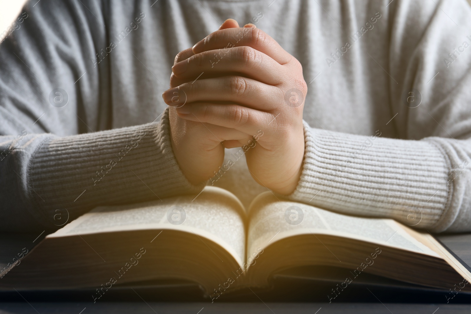 Photo of Woman holding hands clasped while praying over Bible at wooden table, closeup