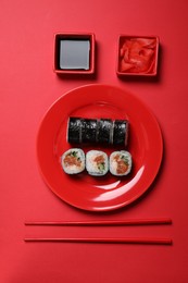 Photo of Tasty sushi rolls, soy sauce and ginger on red background, flat lay