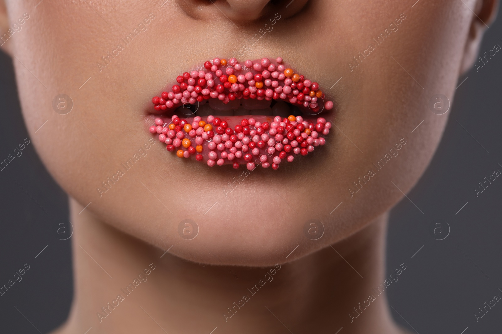 Photo of Young woman with beautiful lips covered confectionery sprinkles on gray background, closeup