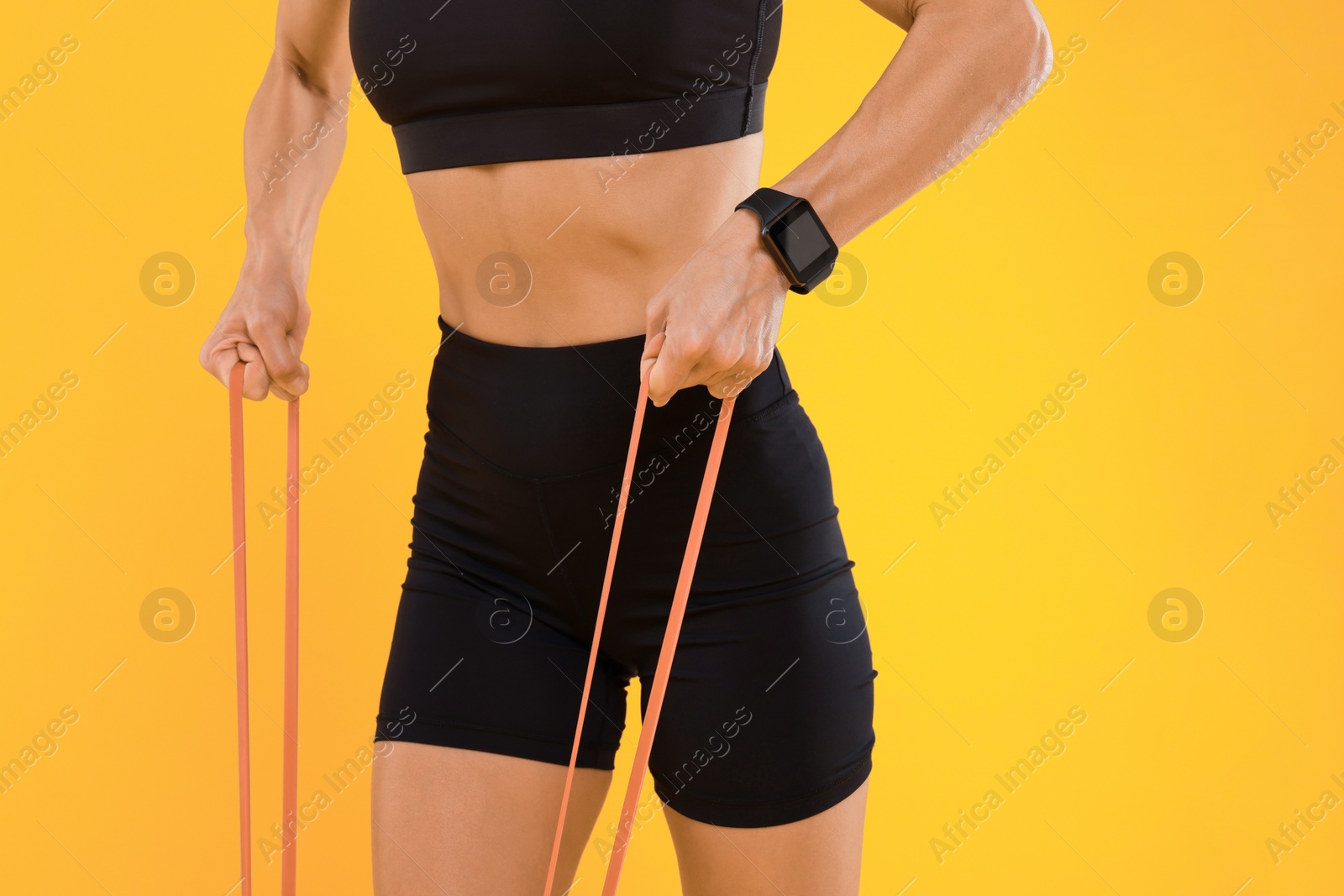 Photo of Woman exercising with elastic resistance band on orange background, closeup