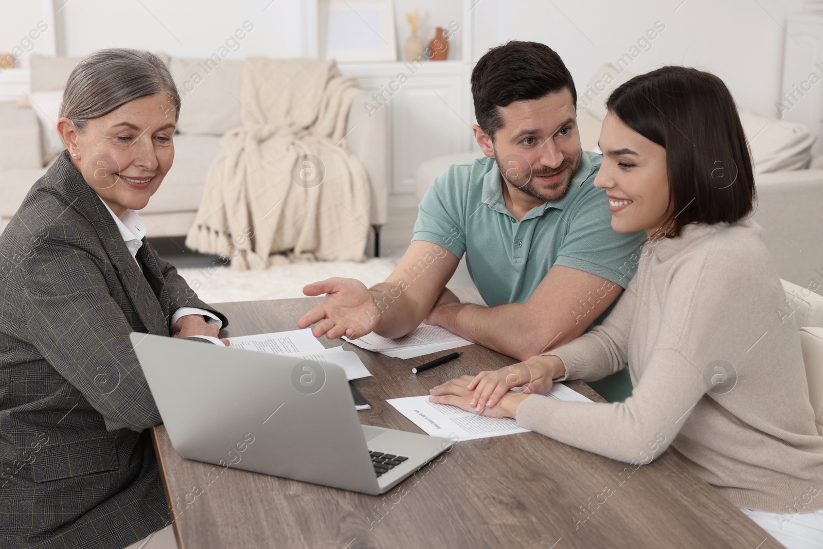 Photo of Young couple consulting insurance agent about pension plan at wooden table indoors