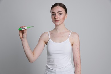 Photo of Woman with rash holding thermometer on light grey background. Monkeypox virus
