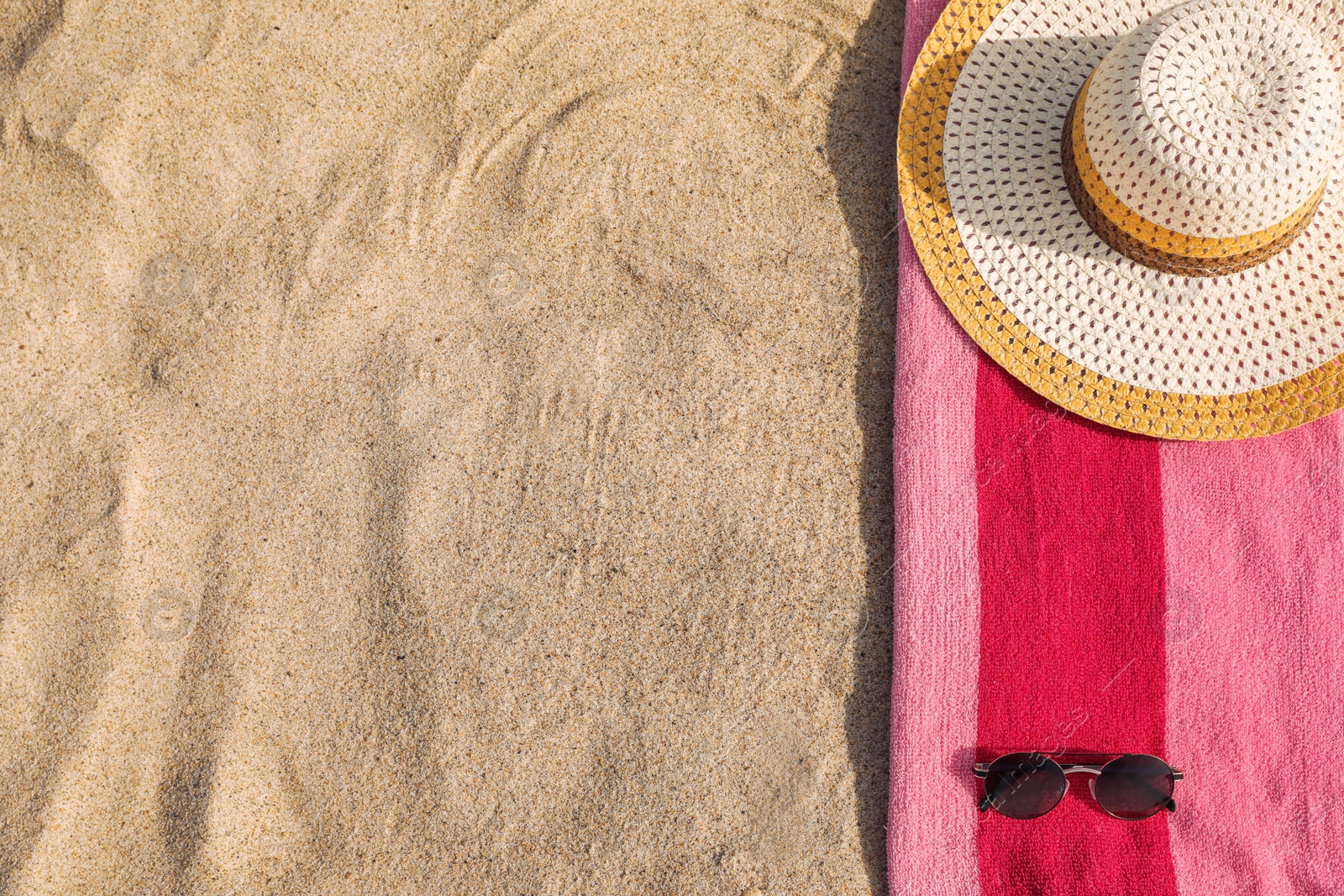 Photo of Beach towel with straw hat and sunglasses on sand, flat lay. Space for text