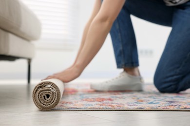 Woman unrolling carpet with beautiful pattern on floor in room, closeup