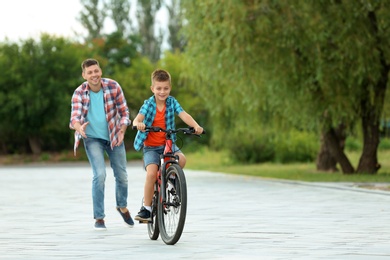 Photo of Dad teaching son to ride bicycle in park