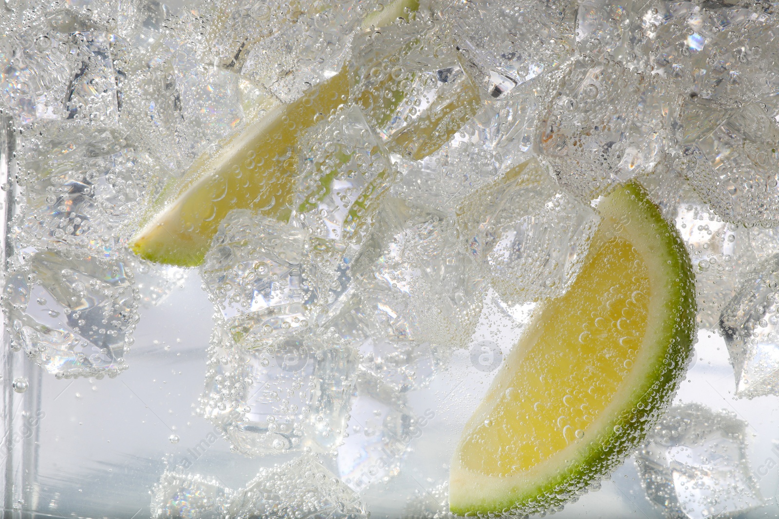 Photo of Juicy lime slices and ice cubes in soda water against white background, closeup