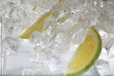 Juicy lime slices and ice cubes in soda water against white background, closeup