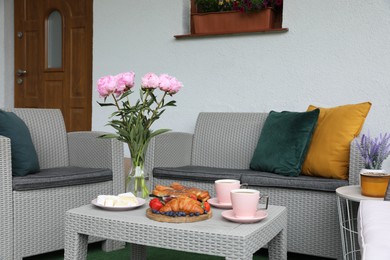 Photo of Morning drink, pastry, berries, cheese and vase with flowers on rattan table. Summer breakfast on terrace