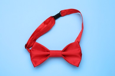 Stylish red bow tie on light blue background, top view