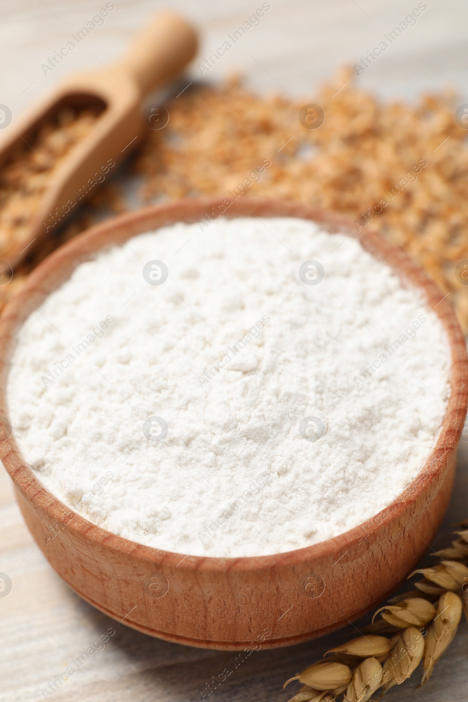 Photo of Bowl with wheat flour and spikelet on wooden table, closeup