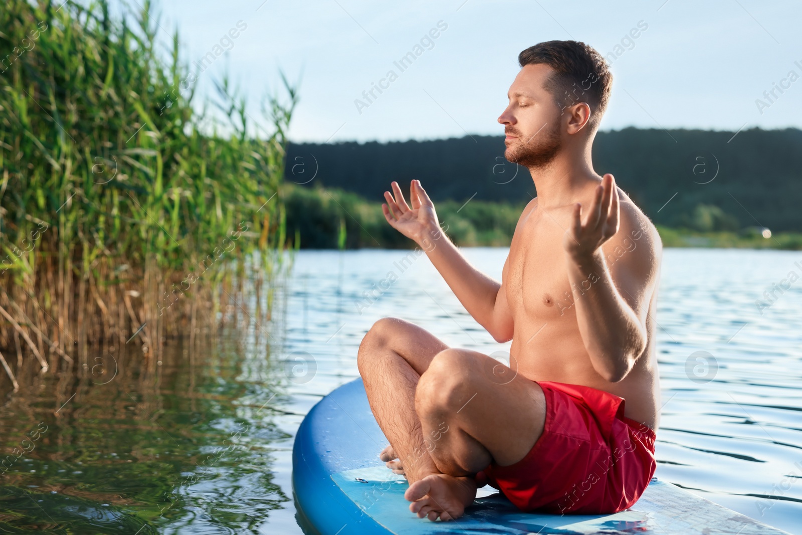 Photo of Man meditating on light blue SUP board on river at sunset