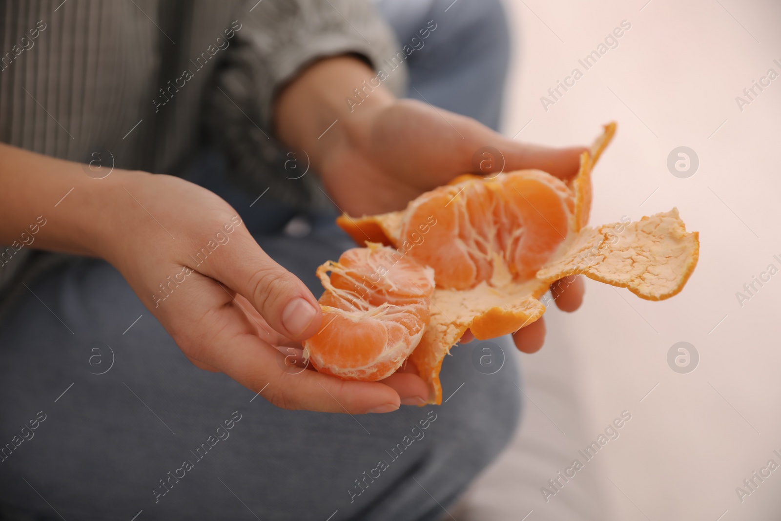Photo of Woman peeling fresh tangerine on blurred background, closeup