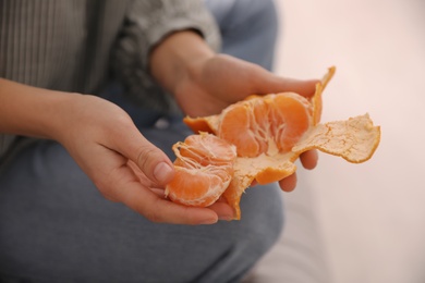 Photo of Woman peeling fresh tangerine on blurred background, closeup