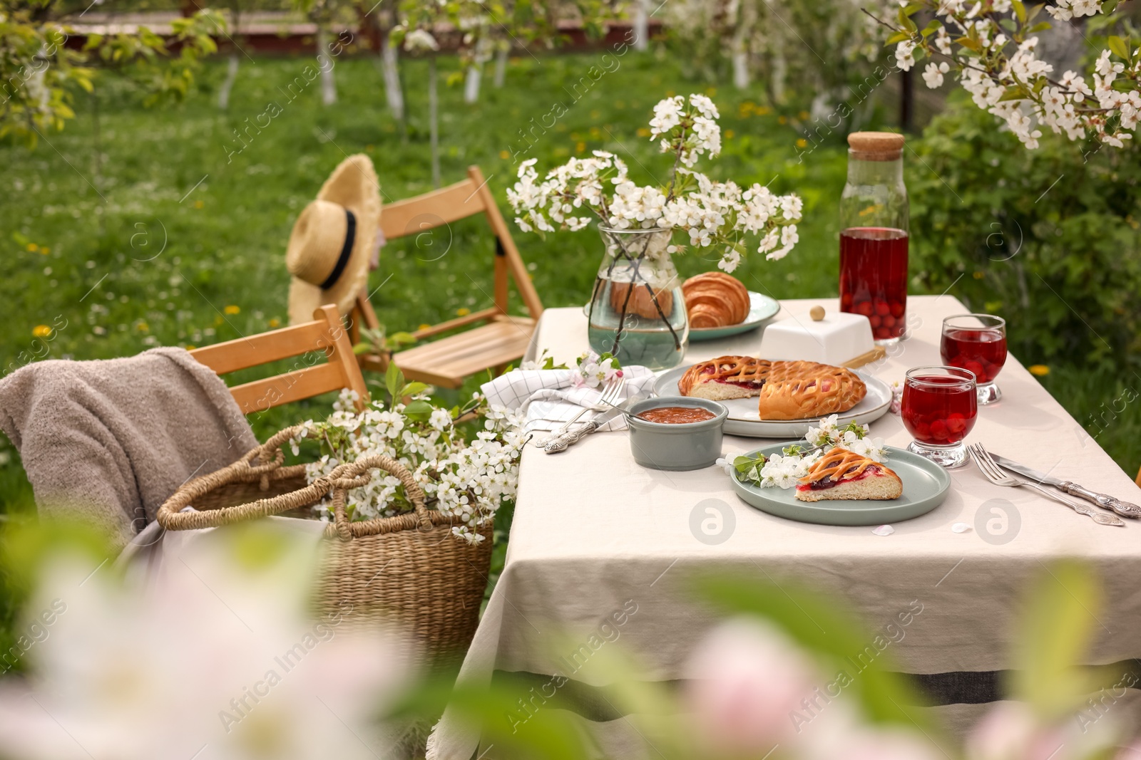 Photo of Stylish table setting with beautiful spring flowers, fruit drink and pie in garden