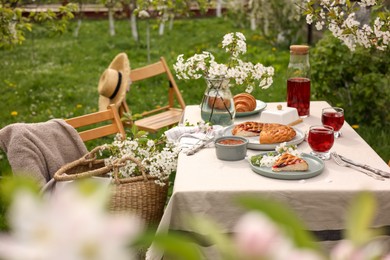 Stylish table setting with beautiful spring flowers, fruit drink and pie in garden