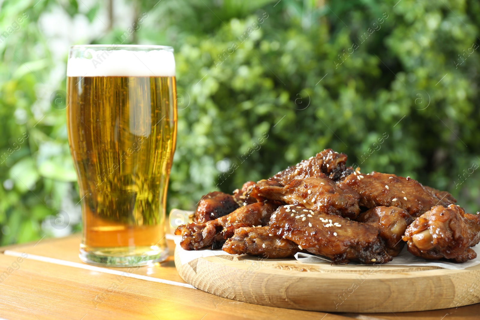 Photo of Tasty roasted chicken wings and glass of beer on wooden table, closeup
