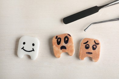 Photo of Clean and dirty plastic teeth with faces, dental tools on white wooden table, flat lay