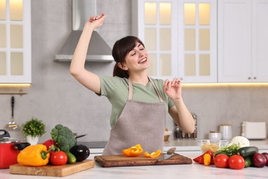 Happy young housewife having fun while cooking at white marble table in kitchen