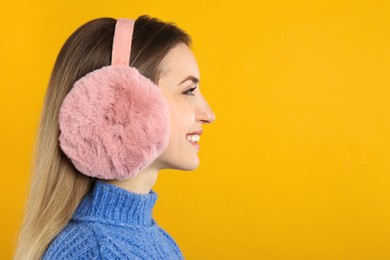 Photo of Happy woman wearing warm earmuffs on yellow background, space for text