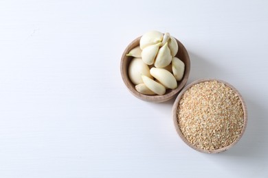 Photo of Dehydrated garlic granules and peeled cloves on white table, flat lay. Space for text