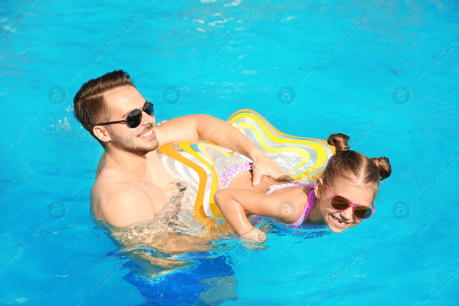 Photo of Father teaching daughter to swim with inflatable star in pool on sunny day