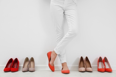 Photo of Woman trying on different shoes near white wall, closeup