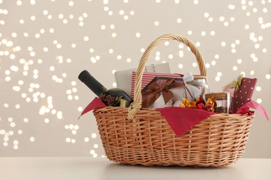 Wicker basket with gifts, wine and food against blurred festive lights. Space for text