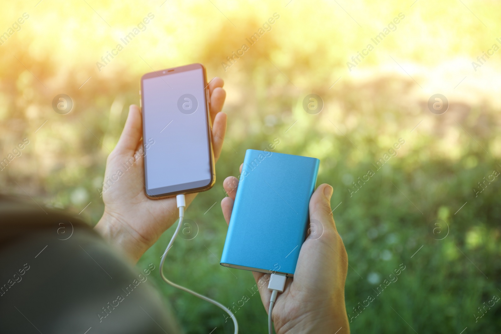 Photo of Woman charging smartphone with power bank in forest, closeup