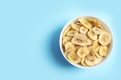 Photo of Bowl with banana slices on color background, top view with space for text. Dried fruit as healthy snack