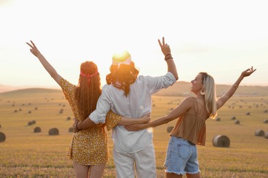 Photo of Hippie friends showing peace signs in field, back view