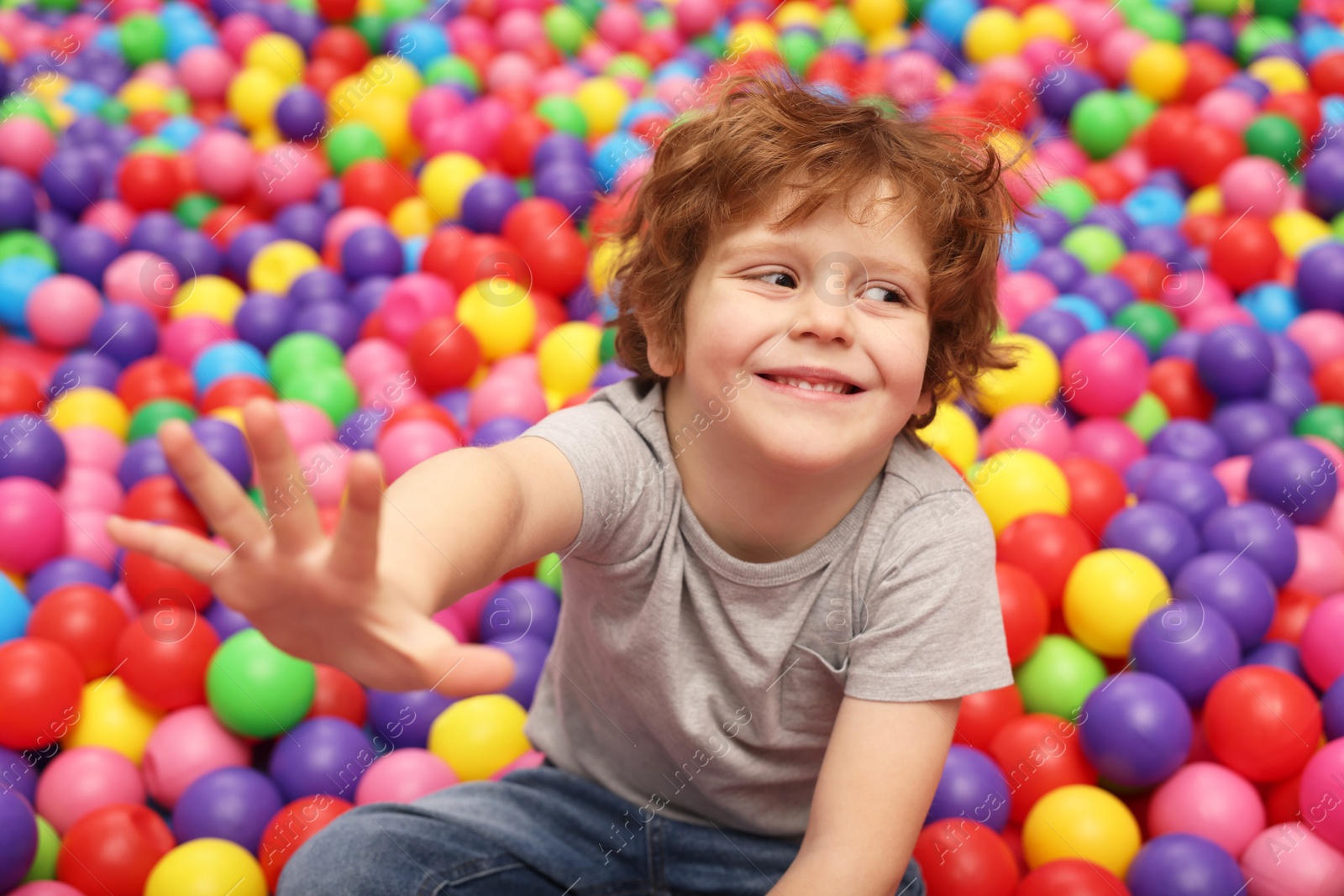 Photo of Happy little boy sitting on colorful balls in ball pit