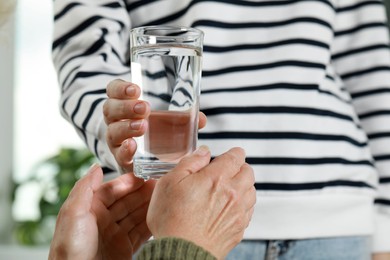 Photo of Caregiver giving water to elderly woman at home, closeup