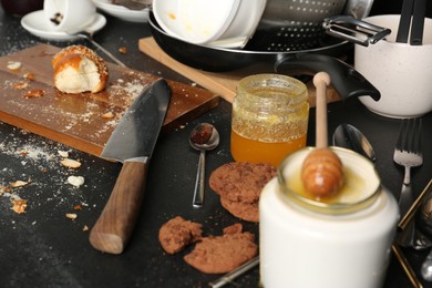 Many dirty utensils, dishware and food leftovers on black countertop. Mess in kitchen