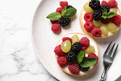 Delicious tartlets with berries on white marble table, top view