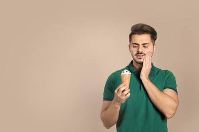 Emotional young man with sensitive teeth and ice cream on color background. Space for text