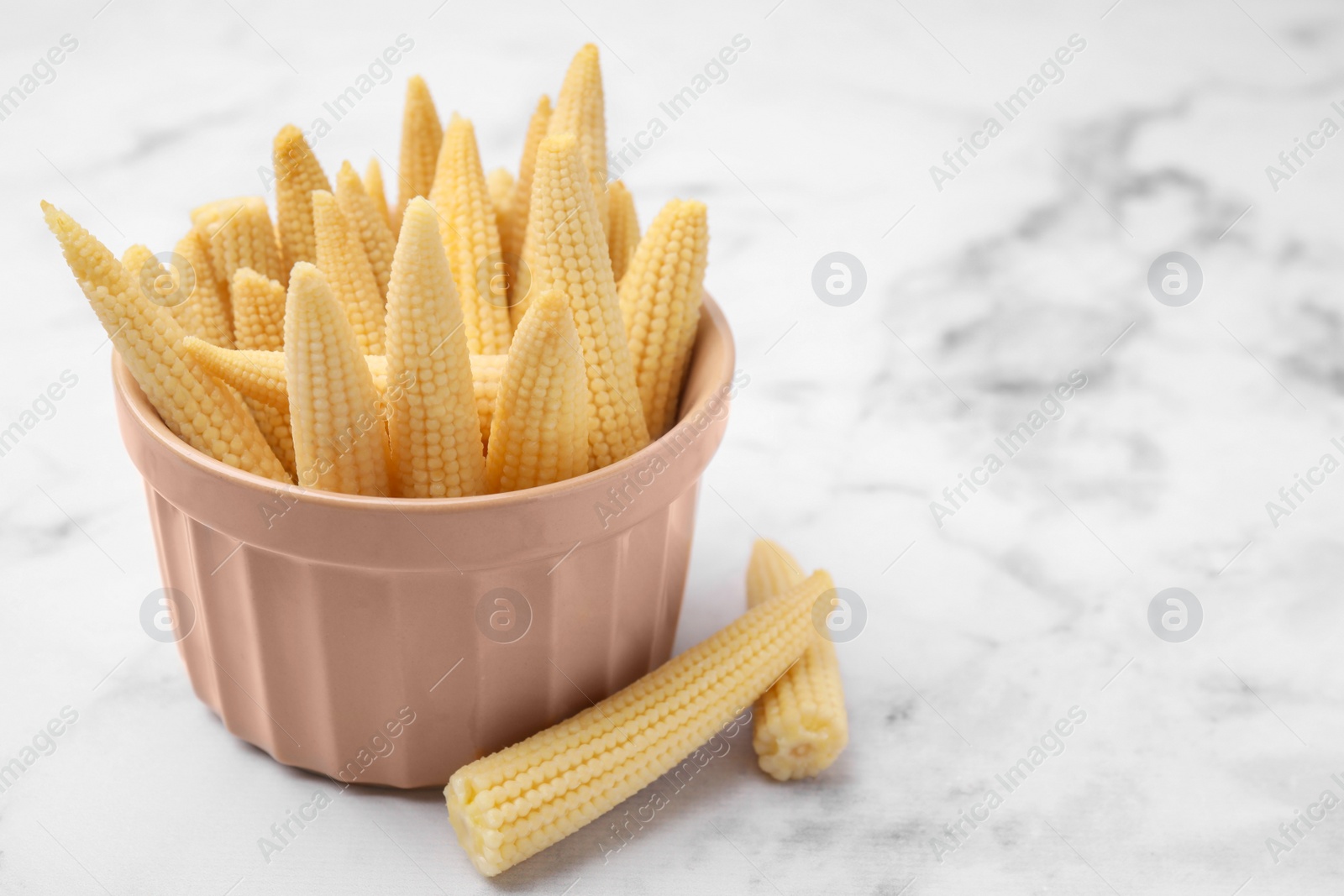 Photo of Bowl and pickled baby corn on white marble table, space for text