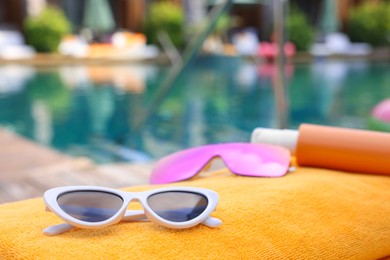 Photo of Sunglasses and sunscreen on beach towel near outdoor swimming pool at luxury resort, closeup. Space for text